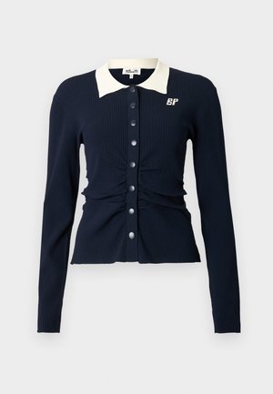 Tengerészkék bordázott hosszú ujjú kardigán fehér gallérral, ráncolt részlettel és nagy gombokkal az elején, bal oldalon a mellrészen logóval.