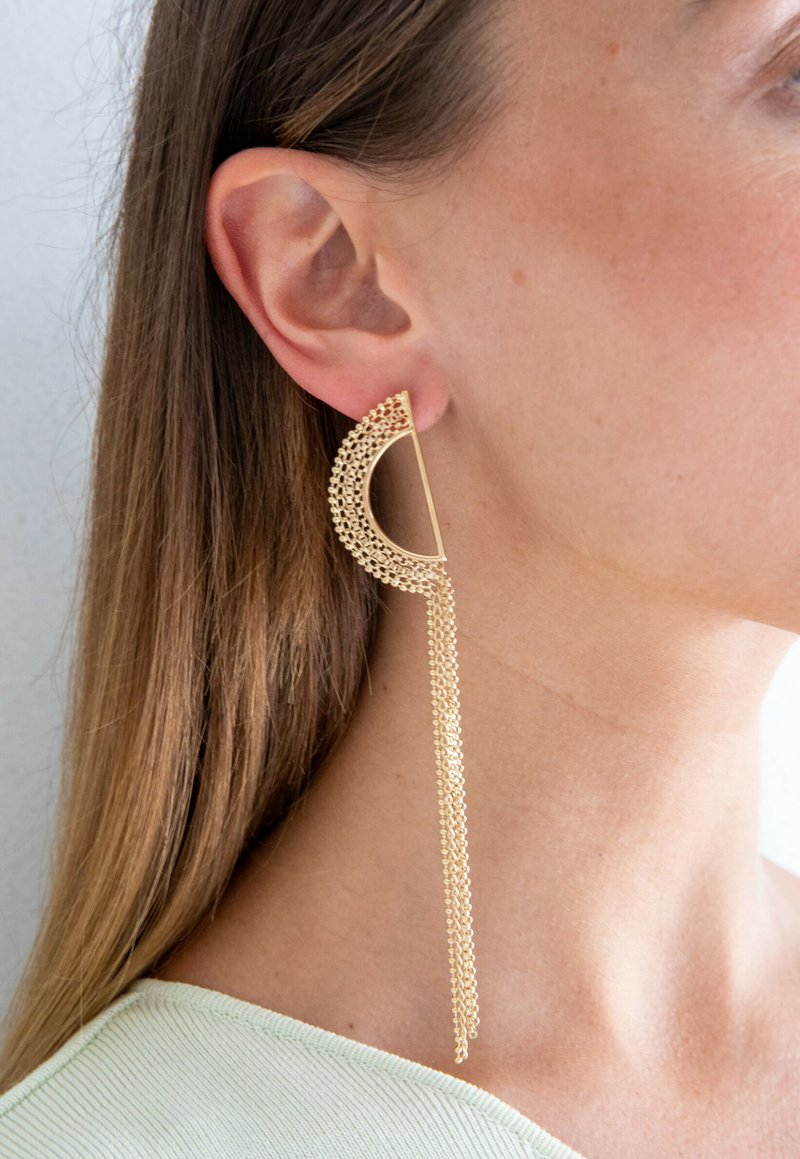 Gouden oorbellen in een halvemaanvorm met een gestructureerd patroon, bevestigd met een ketting die onder de oorlel hangt, met een gepolijste afwerking.