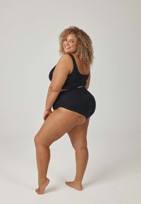 Czarny, bezszwowy zestaw składający się z biustonosza i wysokich majtek. Tkanina wydaje się gładka o matowym wykończeniu; minimalistyczny design bez widocznych elementów metalowych.