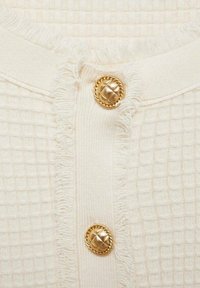 Sweter z fakturowanego kremowego materiału z tkanym wzorem w kratkę, z postrzępionymi brzegami i dwoma złotymi guzikami o plecionym wzorze.