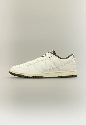 Biały niski sneaker Nike z czarną podeszwą, perforowanym noskiem, sznurówkami i czarną podszewką wewnętrzną, pokazany z boku na neutralnym tle.