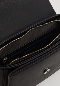 Cartera de piel negra texturizada abierta para mostrar un compartimento con cremallera dorada y múltiples ranuras para tarjetas en el interior.