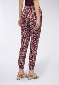 Pantaloni a stampa floreale color bordeaux con una vestibilità rilassata, vita elastica e polsini affusolati. Abbinati a sandali con tacco a blocco beige.