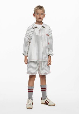 Tenue rayée blanche et marine composée d'une chemise à manches longues et d'un short, avec des détails de couture rouges et des chaussettes grises à rayures rouges.