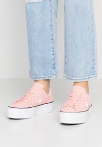 Baskets compensées en suède rose avec détail étoile blanche, dotées d'un design à lacets et d'une semelle en caoutchouc blanche, associées à un jean court bleu clair.