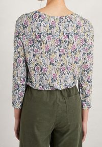 Blusa floreale con maniche lunghe, caratterizzata da una stampa multicolore su sfondo chiaro. Abbinata a pantaloni in velluto a coste verde oliva.