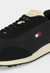 Μαύρο αθλητικό παπούτσι Tommy Jeans με μπεζ γλώσσα και σόλα, μαύρα κορδόνια και λογότυπο Tommy Jeans με τη σημαία στην πλαϊνή επένδυση.