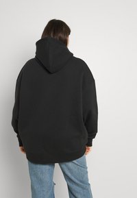 Felpa nera oversized con un grande cappuccio a punta e spalle scese, abbinata a jeans chiari strappati. Tessuto in cotone liscio.