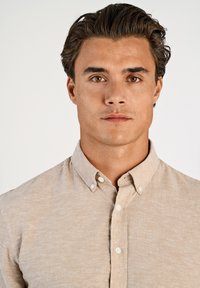 Beige overhemd met knopen en een subtiele structuur en een kraag. Heeft witte knopen en een klassieke pasvorm, geschikt voor casual of nette gelegenheden.