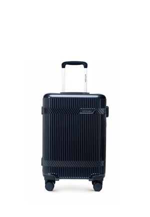 Valise marine compacte à coque rigide avec rainures verticales, quatre roues pivotantes et poignée télescopique déployée.