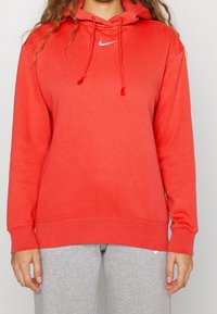 Rode hoodie van een katoenmix, met een voorste kangaroo zak, koordjes en een klein Nike logo op de borst. Gecombineerd met grijze broek.