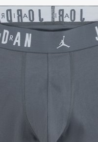 Grå herreshorts med en hvid elastisk talje, der har "Jordan" tekst og logo. Blødt stof og tætsiddende design.