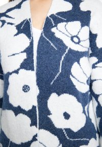 Cardigan lavorato a maglia con un motivo floreale blu e bianco, caratterizzato da una texture morbida, apertura frontale e una vestibilità rilassata.