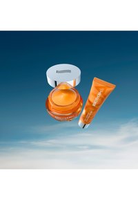 Oransje gelkrem i en klar krukke med en sølvhette, sammen med en matchende oransje tube; begge har stilfulle design og minimal merkevare.