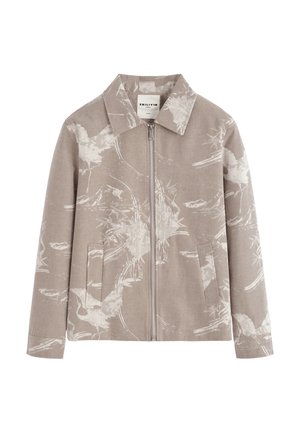 Veste marron clair à fermeture éclair avec col pointu et motif floral blanc subtil, équipée de deux poches avant et de manches longues.