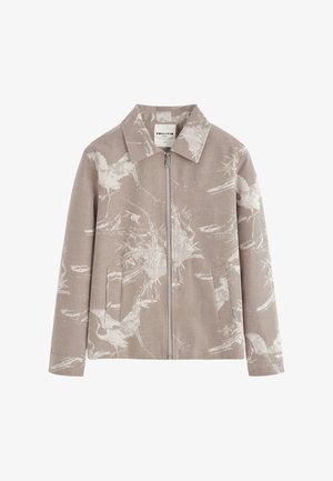 Veste marron clair à fermeture éclair avec col pointu et motif floral blanc subtil, équipée de deux poches avant et de manches longues.