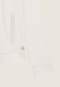 Sweatshirt blanc avec des manches texturées, une poche latérale et une petite étiquette en cuir de marque dans le coin inférieur. Poignets en côte doux.