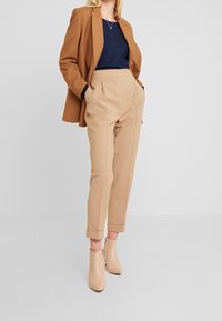 Brązowa marynarka na granatowej bluzce, zestawiona z beżowymi, wysokim stanem i mankietami spodniami oraz botkami w jasnym beżowym odcieniu.