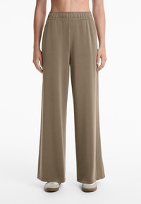 Wide-leg trousers in a soft taupe fabric, featuring an elastic waistband and side slits, with a smooth texture and relaxed fit.