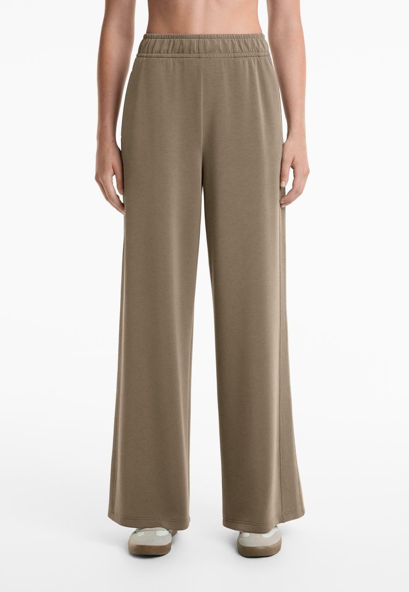 Wide-leg trousers in a soft taupe fabric, featuring an elastic waistband and side slits, with a smooth texture and relaxed fit.