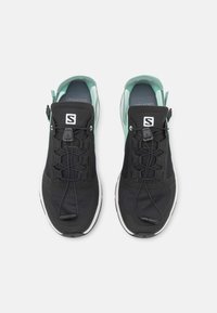 Zapatillas deportivas negras y verde menta con parte superior de malla transpirable, cordones integrados y una suela blanca acolchada.