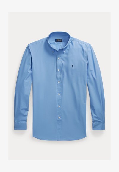 Ανοιχτό μπλε μακρυμάνικο πουκάμισο με κουμπιά και κλασικό γιακά, με μικρό σκούρο λογότυπο στο αριστερό στήθος και λευκά κουμπιά.