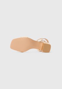 Nude high heel sandal with thin straps, square heel, and textured rubber sole. Smooth upper material and minimalistic design.
