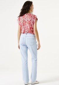 Top de patrón floral en rojo y blanco con mangas cortas, combinado con jeans de textura azul claro con un diseño sutil y bolsillos traseros.