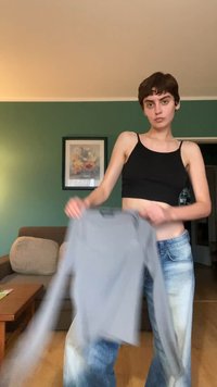 Sort croptop og grå langærmet skjorte holdt af en person, parret med lyseblå denim jeans. Simpelt design, blød tekstur.