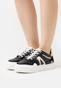 Baskets noir et blanc avec un mélange de cuir et de daim, une semelle épaisse blanche et des accents latéraux contrastants. Les lacets sont blancs.