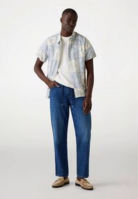 Kortärmad skjorta i ljusblått med blommönster, kombinerad med löst sittande blå jeans och beige slip-on skor.