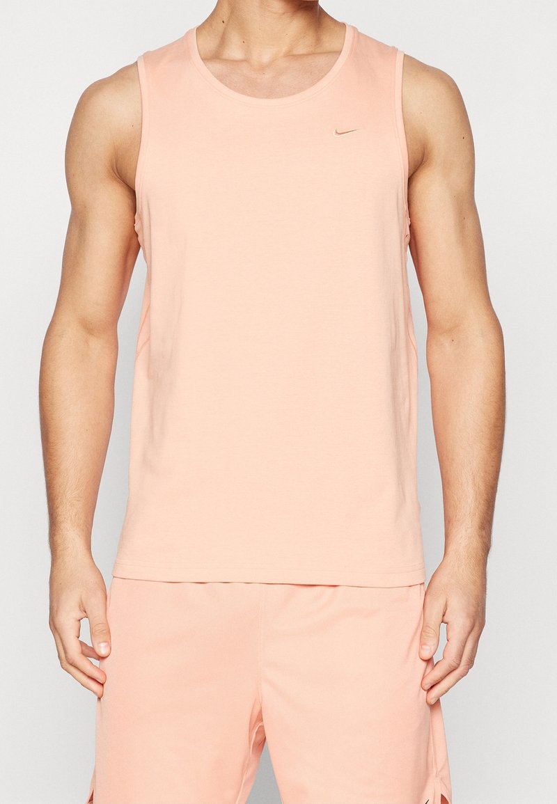 Homme portant un débardeur Nike sans manches pêche clair et un short assorti, debout devant un fond clair uni.