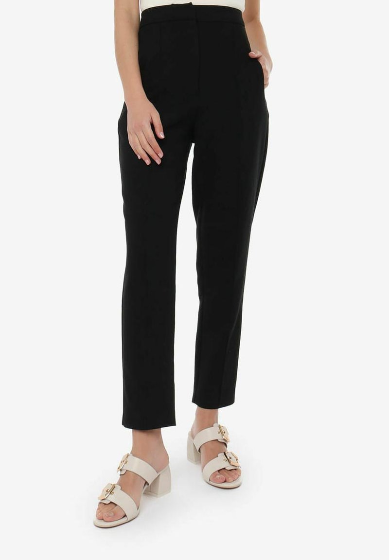 Pantaloni neri su misura con una vestibilità slim, vita alta, tasche laterali e un tessuto liscio. Abbinati a sandali bianchi con tacco a blocco e dettagli dorati.