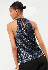 Sort glitrende top med halterneck-design, draperet ryg med nøglehulsskæring og en tekstureret, glimtende overflade.