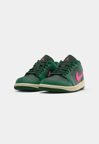 Sneakers verdes em pele apresentam um swoosh e um logótipo rosa, com uma entressola bege e sola de borracha preta. Os atacadores são pretos e o design é de cano baixo.