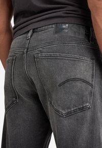 Jeans de mezclilla negros para hombre con una silueta ajustada, que cuentan con un parche de logo de cuero, bolsillos traseros y costuras en contraste.