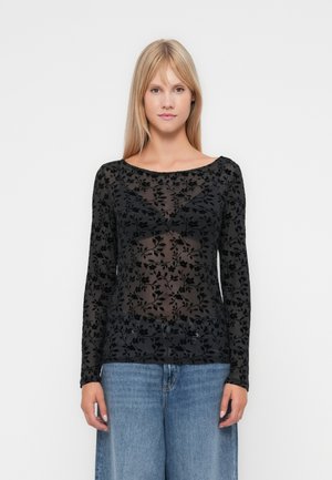Svart langermet topp laget av gjennomsiktig stoff med blomsterdesign. Har vid halsutskjæring og er kombinert med lyseblå jeans.