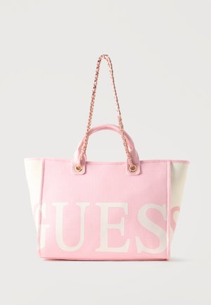 Pink and white tote bag with gold chain and fabric handles, featuring large white "GUESS" lettering across the front.