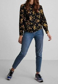 Black blouse with floral print in pink and yellow, buttoned front, long sleeves, paired with light blue jeans and athletic shoes.