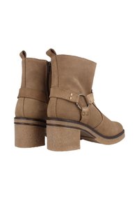 Botas de tobillo de ante marrón con un tacón robusto, acento de anillo de metal y cremallera lateral. Presentan una correa ancha alrededor del tobillo con botón a presión.