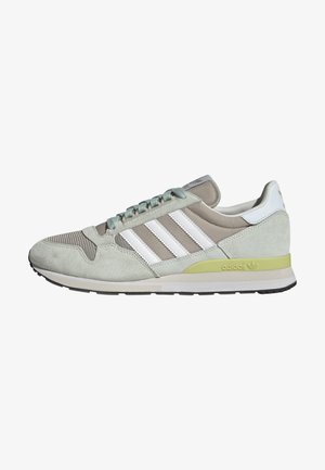 Baskets Adidas gris clair et beige avec des bandes blanches, un accent de semelle vert clair et une semelle noire, vues de profil côté gauche.