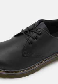 Scarpa in pelle nera con punta rotonda, caratterizzata da sei occhielli, lacci neri e cuciture gialle lungo la suola. Fodera interna testurizzata.