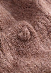 Gros plan sur un tissu en tricot marron doux et duveteux avec un petit détail en tricot texturé en forme de cœur au centre.