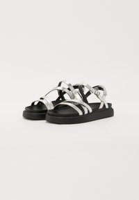 Sandalias plateadas con tiras y suela de goma negra. Presenta múltiples tiras cruzadas y un cierre de hebilla para un ajuste seguro. Textura suave en toda la superficie.