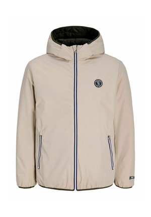 Veste à capuche beige avec fermeture éclair sur le devant, deux poches zippées, poignets élastiques et un patch rond noir avec logo sur la poitrine.