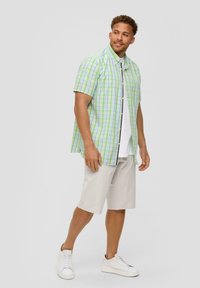 Kortebloemig geruit shirt in groen en blauw, gecombineerd met beige shorts en witte sneakers. Het heeft knopen en een ontspannen pasvorm.