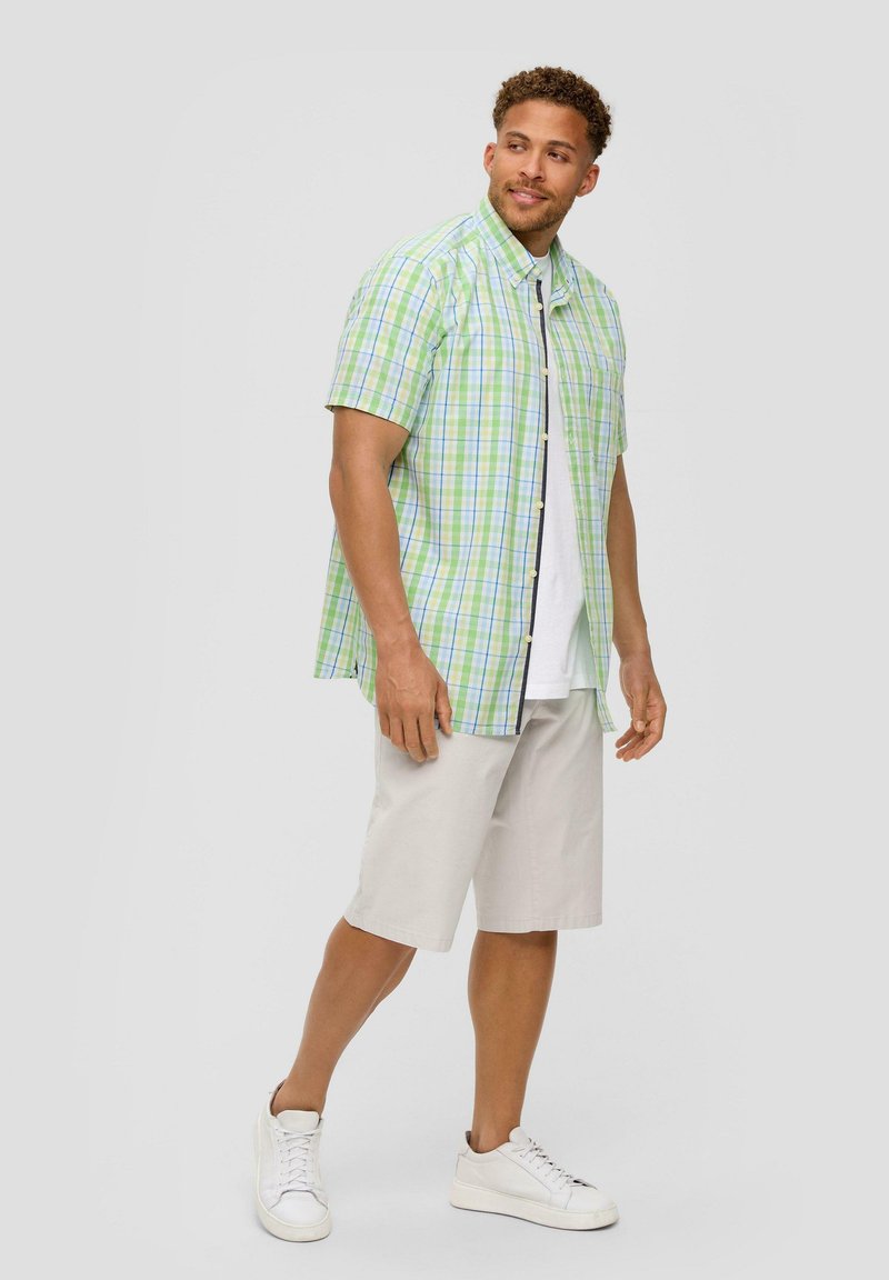 Kortebloemig geruit shirt in groen en blauw, gecombineerd met beige shorts en witte sneakers. Het heeft knopen en een ontspannen pasvorm.