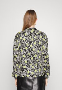 Blusa con stampa floreale che presenta fiori neri e gialli su un motivo leopardato bianco. Maniche lunghe con vestibilità morbida e colletto.