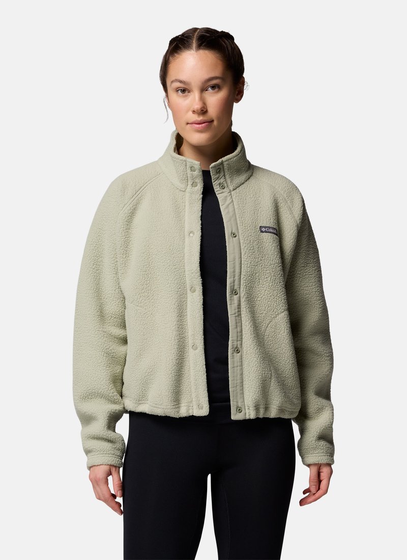 Woman wearing a light green fleece jacket over a black top, standing against a plain white background.