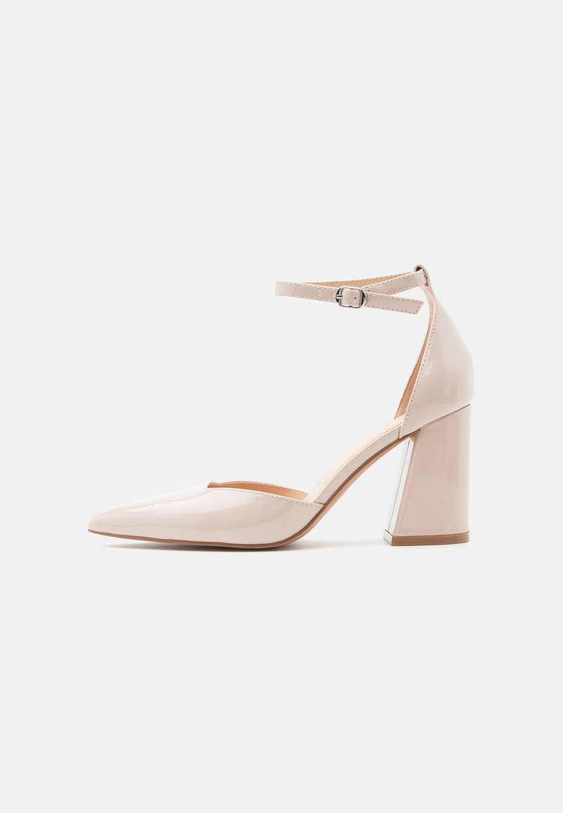 Chaussure à talon haut en cuir verni beige avec bout pointu et bride à la cheville ornée d'une petite boucle, vue de côté.